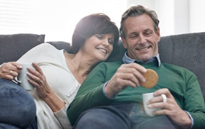 Smiling middle age couple on sofa dunking McVitie's digestive biscuits in tea cup