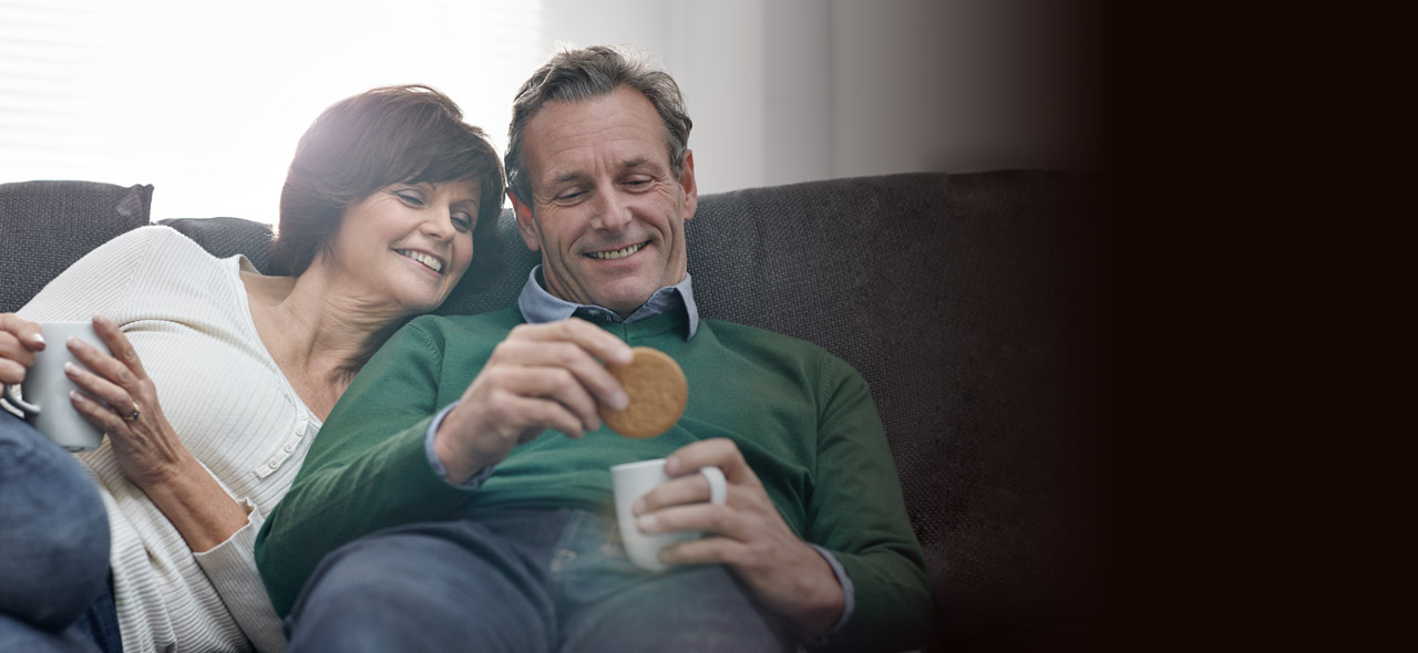 Smiling middle age couple on sofa dunking McVitie's digestive biscuits in tea cup