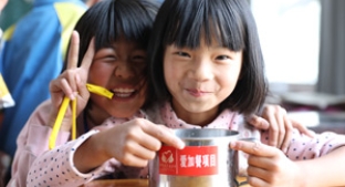 Two smiling Chinese school children eating lunch